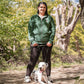 Woman in a green jacket standing with a Dalmatian dog on a path in a park.