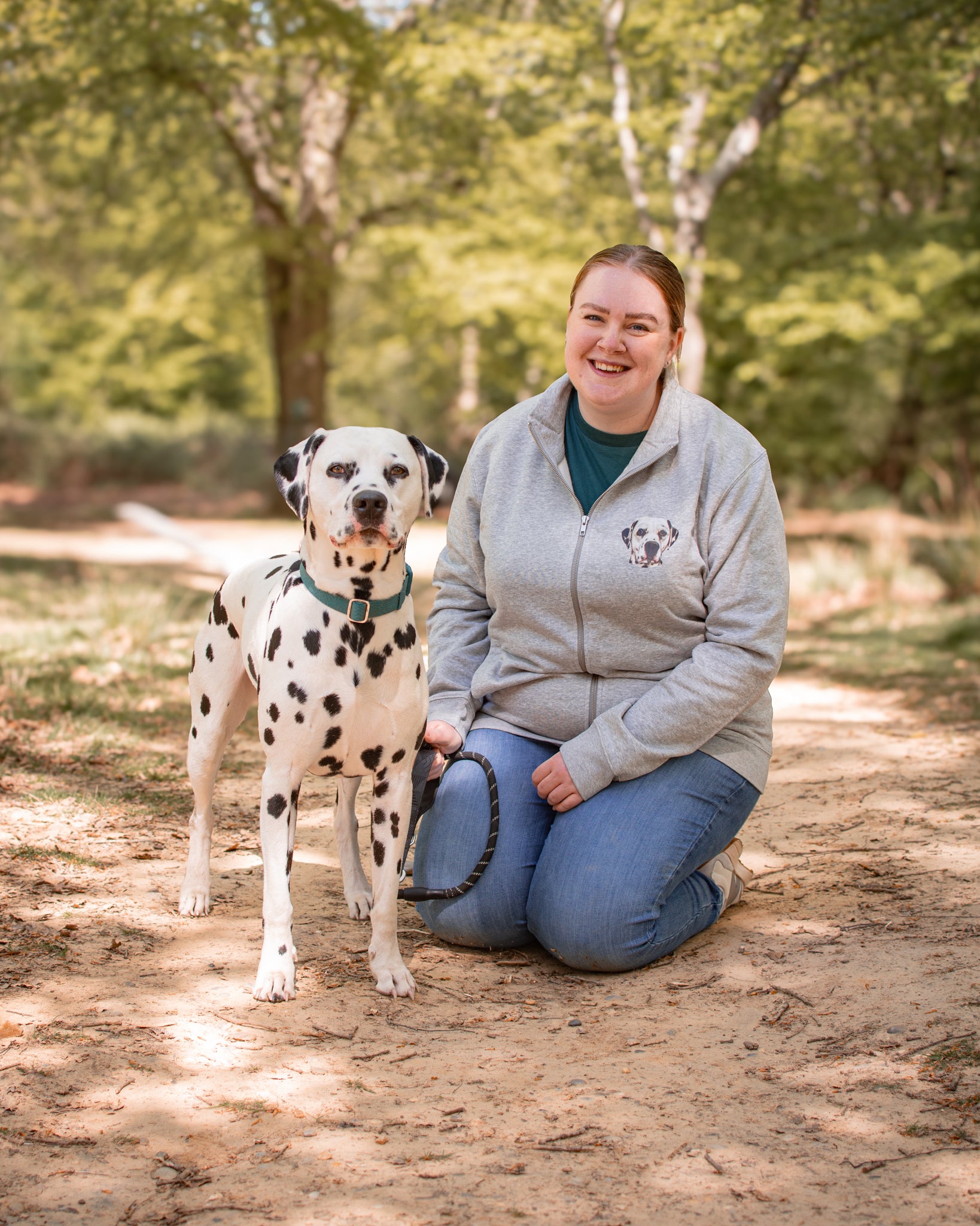 Woman kneeling on a path in a park with a Dalmatian dog.