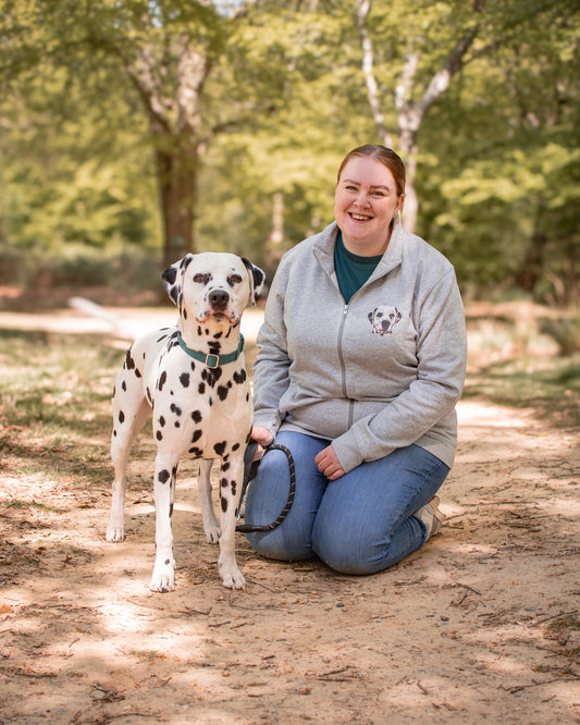 Woman kneeling on a path in a park with a Dalmatian dog.